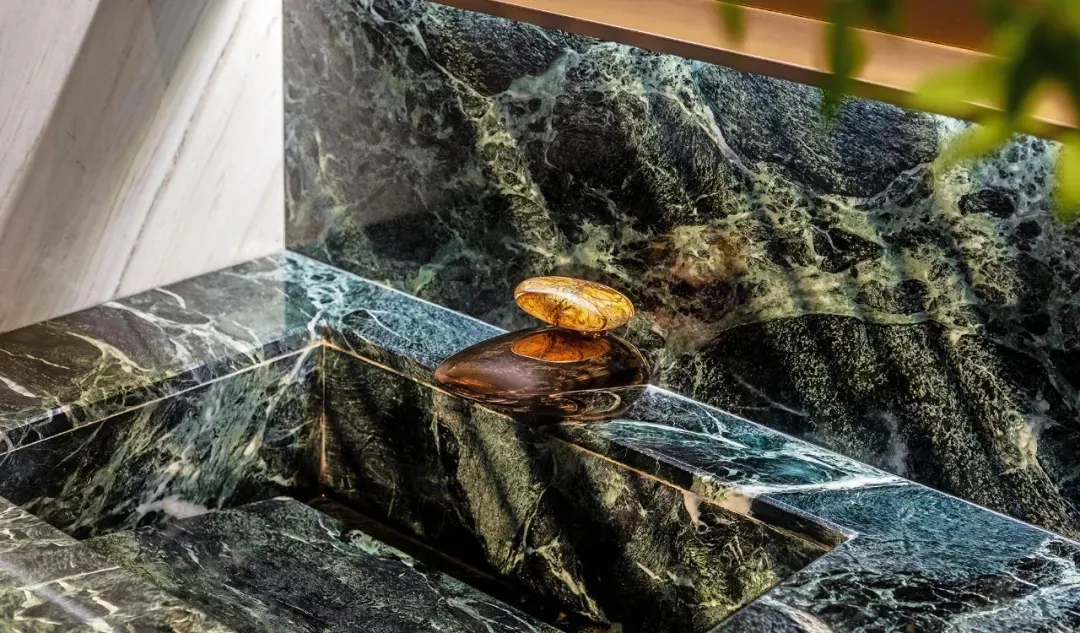Close-up of a modern bathroom showcasing glossy marble tiles with intricate green veins, featuring a sleek, oval-shaped fauce