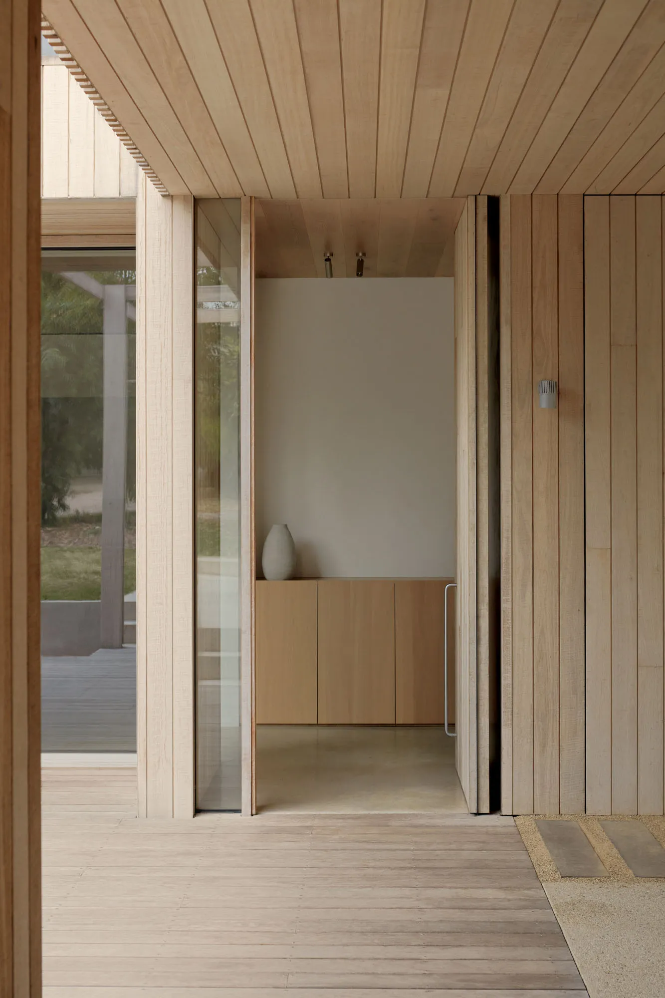 Modern minimalist entryway with wooden walls and large glass window.