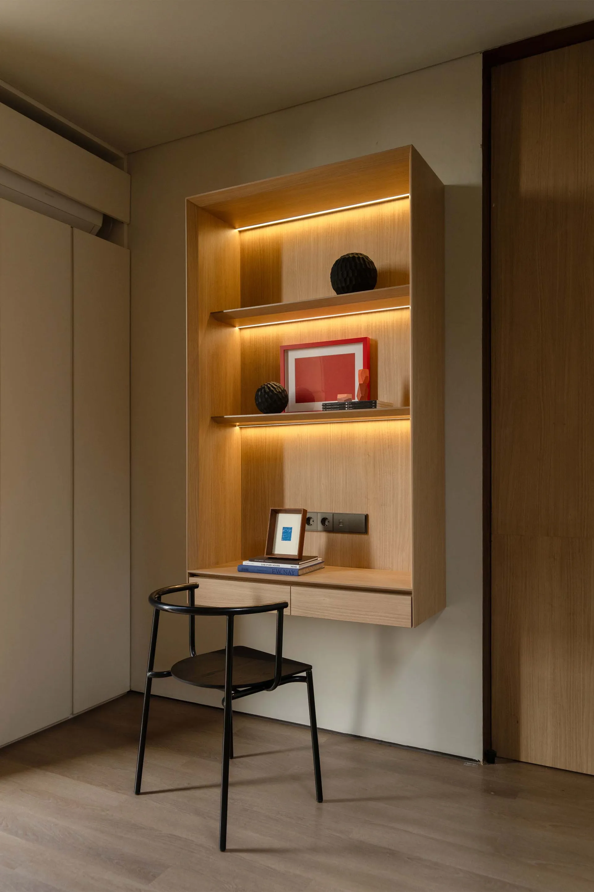 A modern study corner featuring a floating shelf with built-in lighting, black chair, and decorative items.