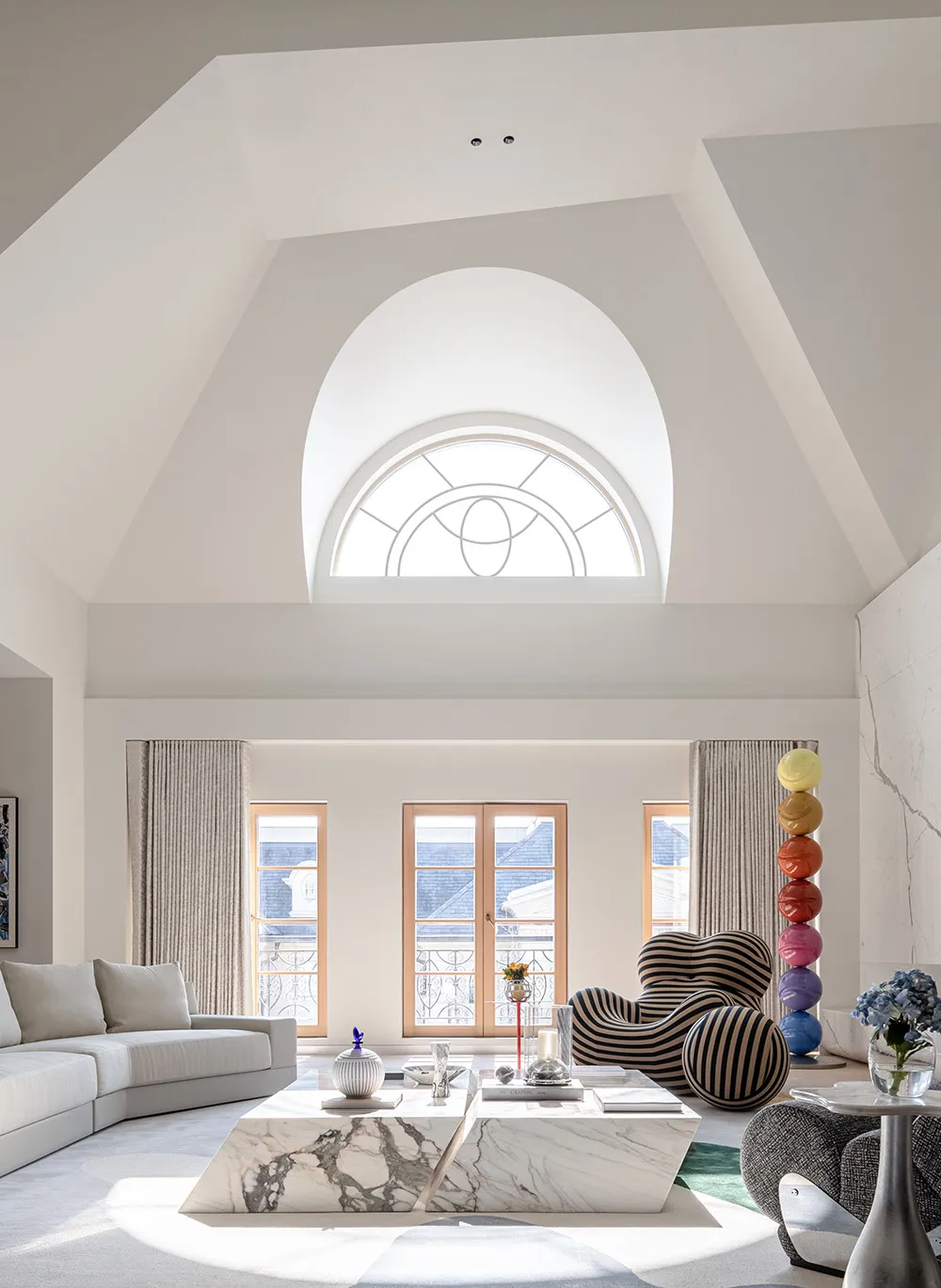 A modern living room with a marble coffee table, striped armchairs, and large arched window.