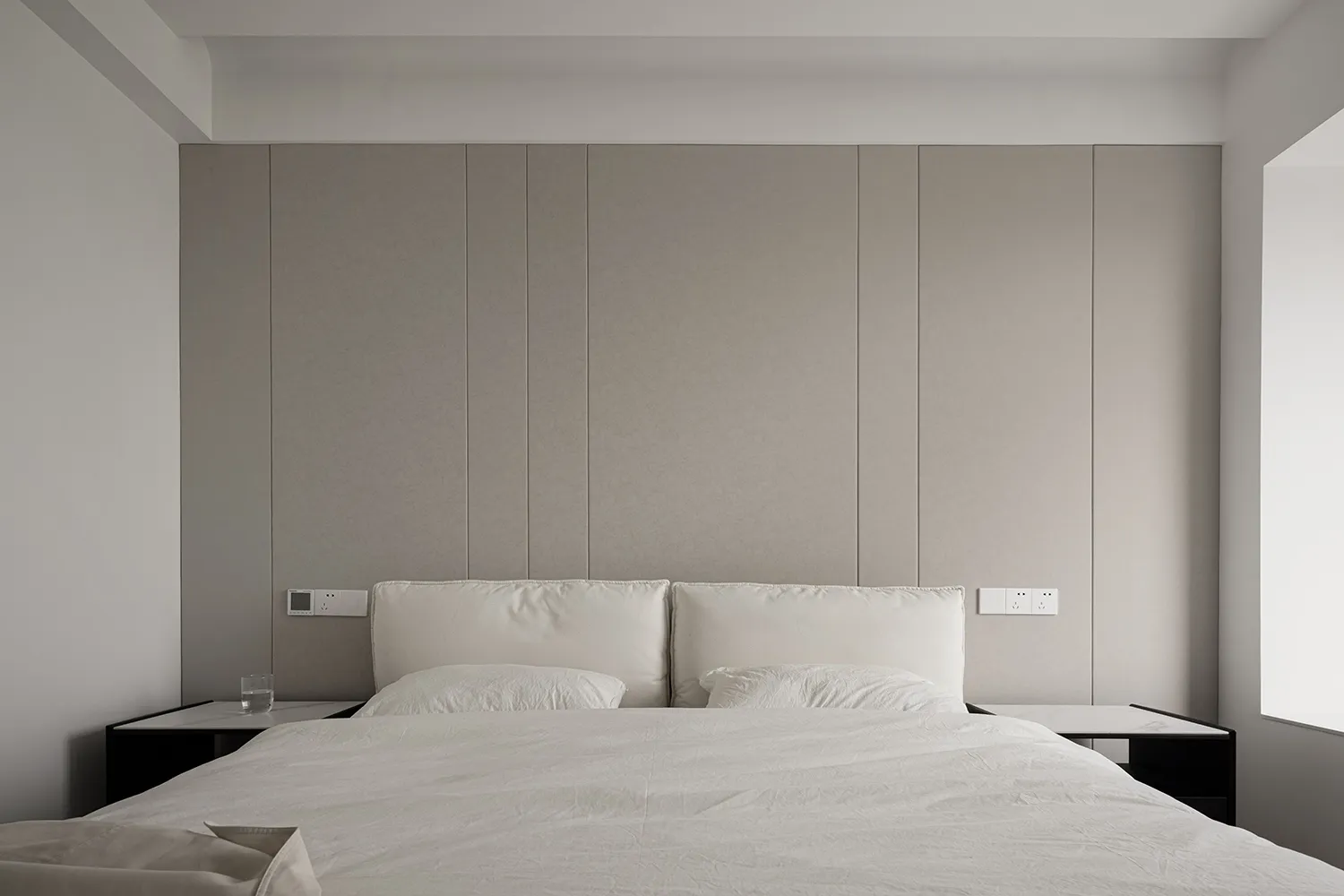 A minimalist bedroom features textured wall panels, a bed with white sheets, and two nightstands.