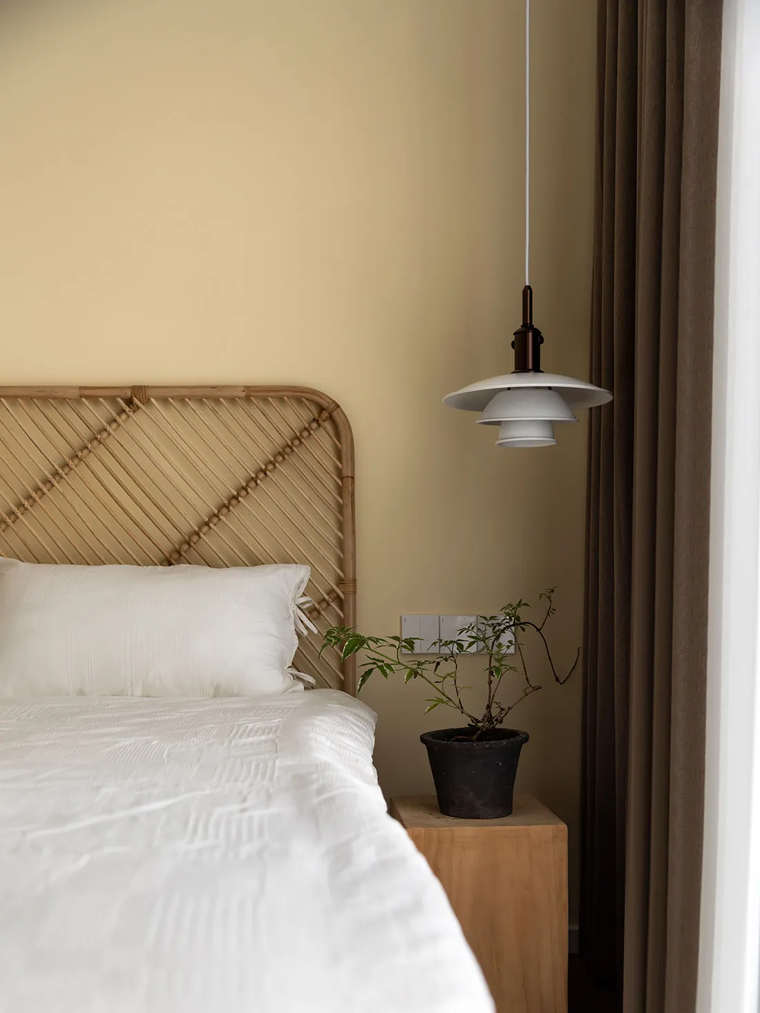 A minimalist bedroom with a wooden headboard, white bedding, and a potted plant on a wooden nightstand.