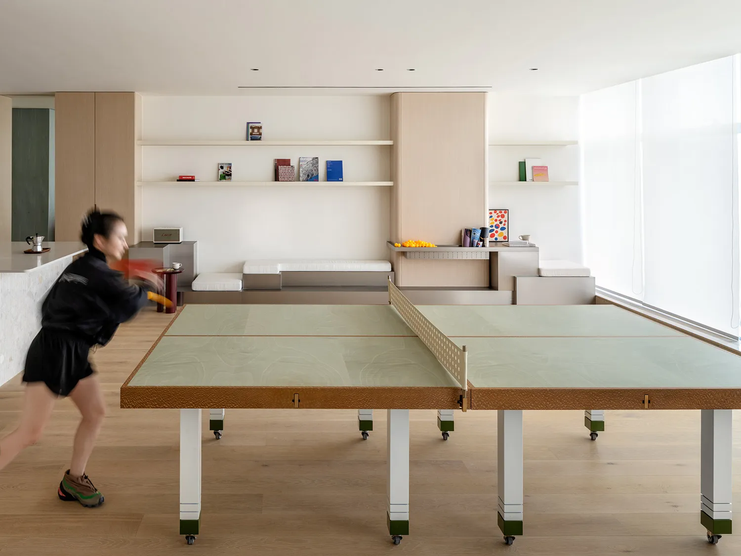 A minimalist living room with a green table tennis table, wooden flooring, and concrete furniture.