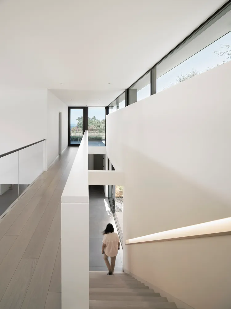 A modern indoor staircase with concrete steps, glass walls, and a view out to the outdoors.