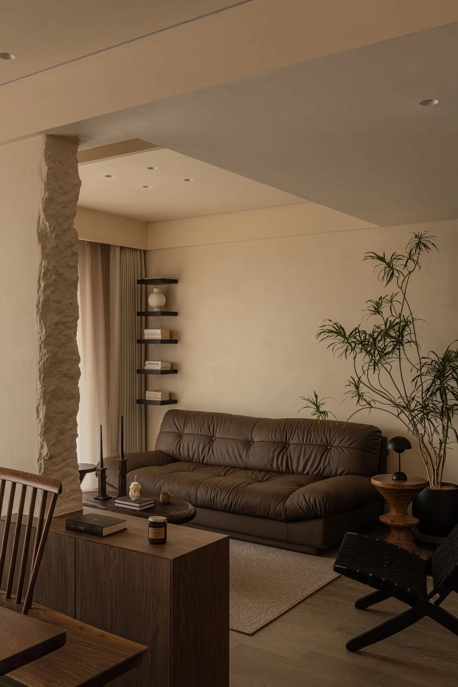 A modern living room featuring a dark leather sofa and wooden furniture, with a minimalist design and warm tones.