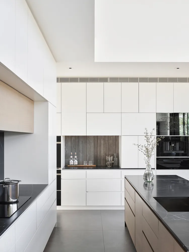 Modern kitchen featuring white marble countertops and aluminum appliances on black marble floor.