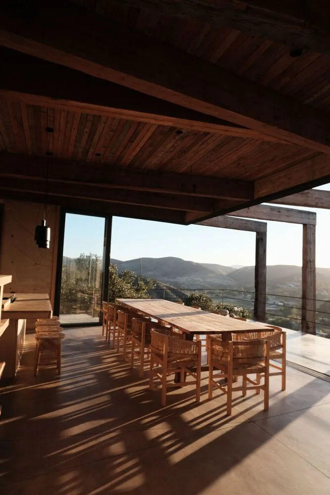 A modern dining room featuring a wooden table and chairs, with a view of hills and mountains.