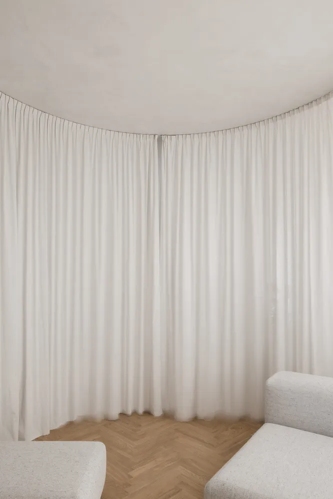A minimalist living room with white curtains and wooden flooring.