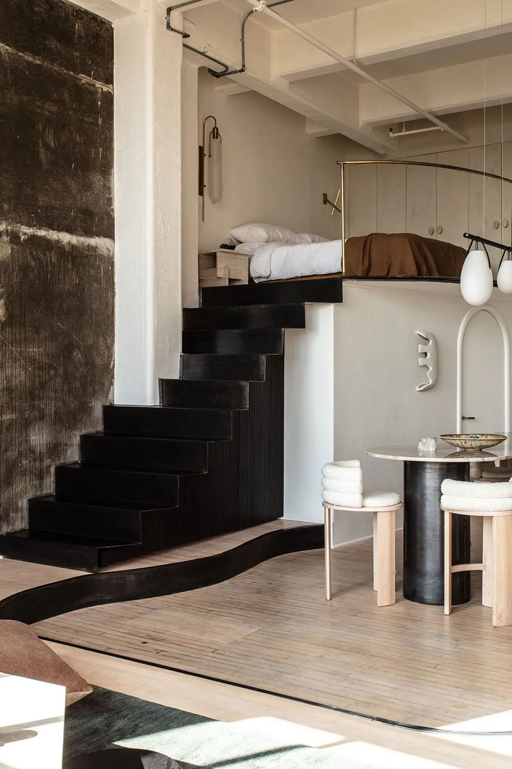 A modern industrial bedroom featuring a metal floating bed on a black staircase against a textured black wall, with a white s