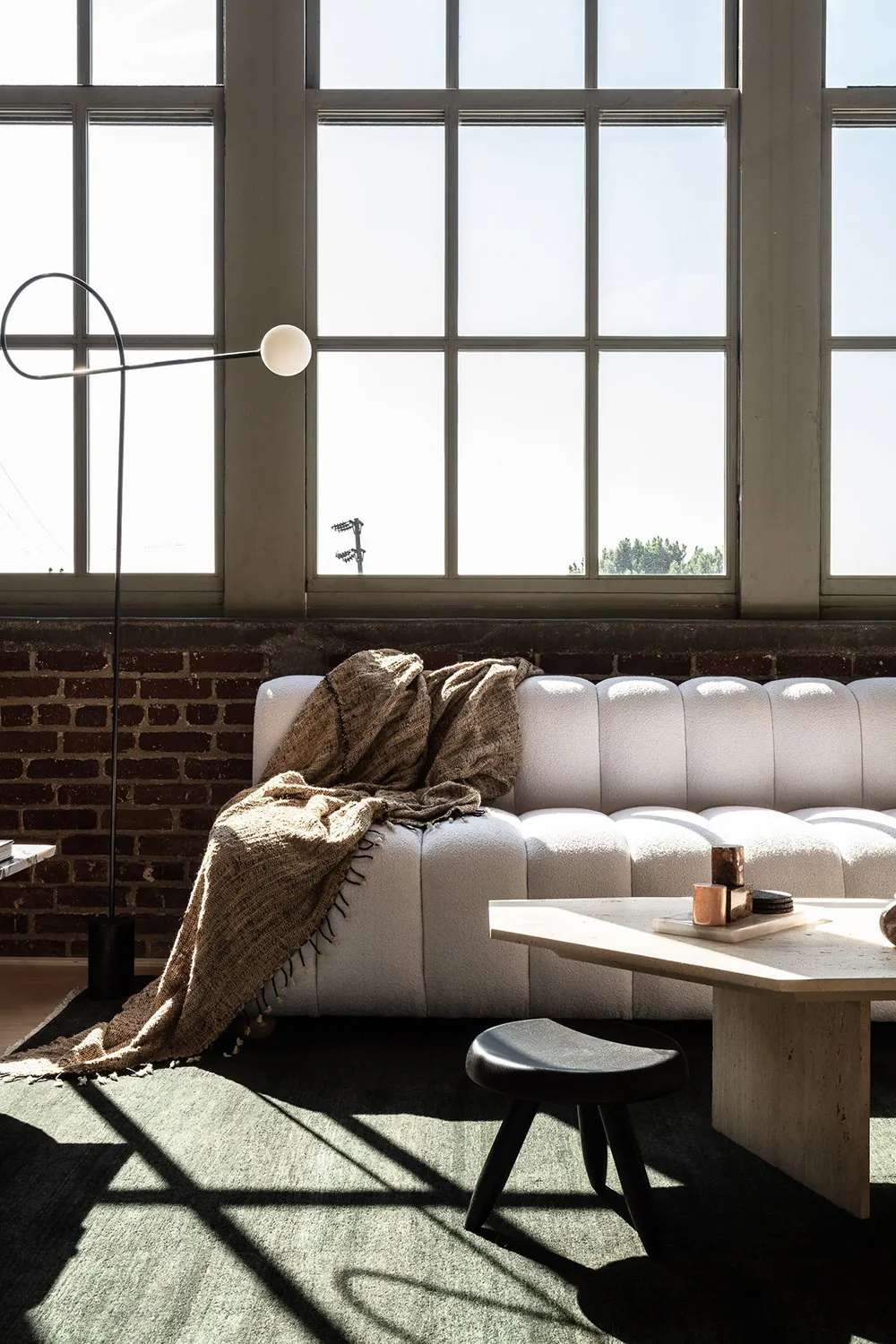 A minimalist living room with a white sofa, brick wall, and large windows.