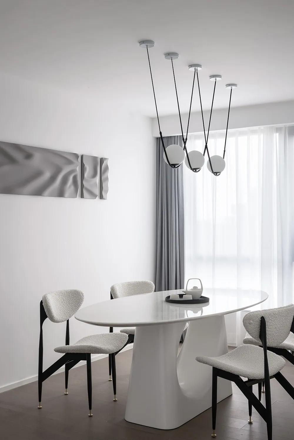 Modern dining room featuring a sleek, white oval table with four chairs, minimalistic design, and hanging pendant lights.