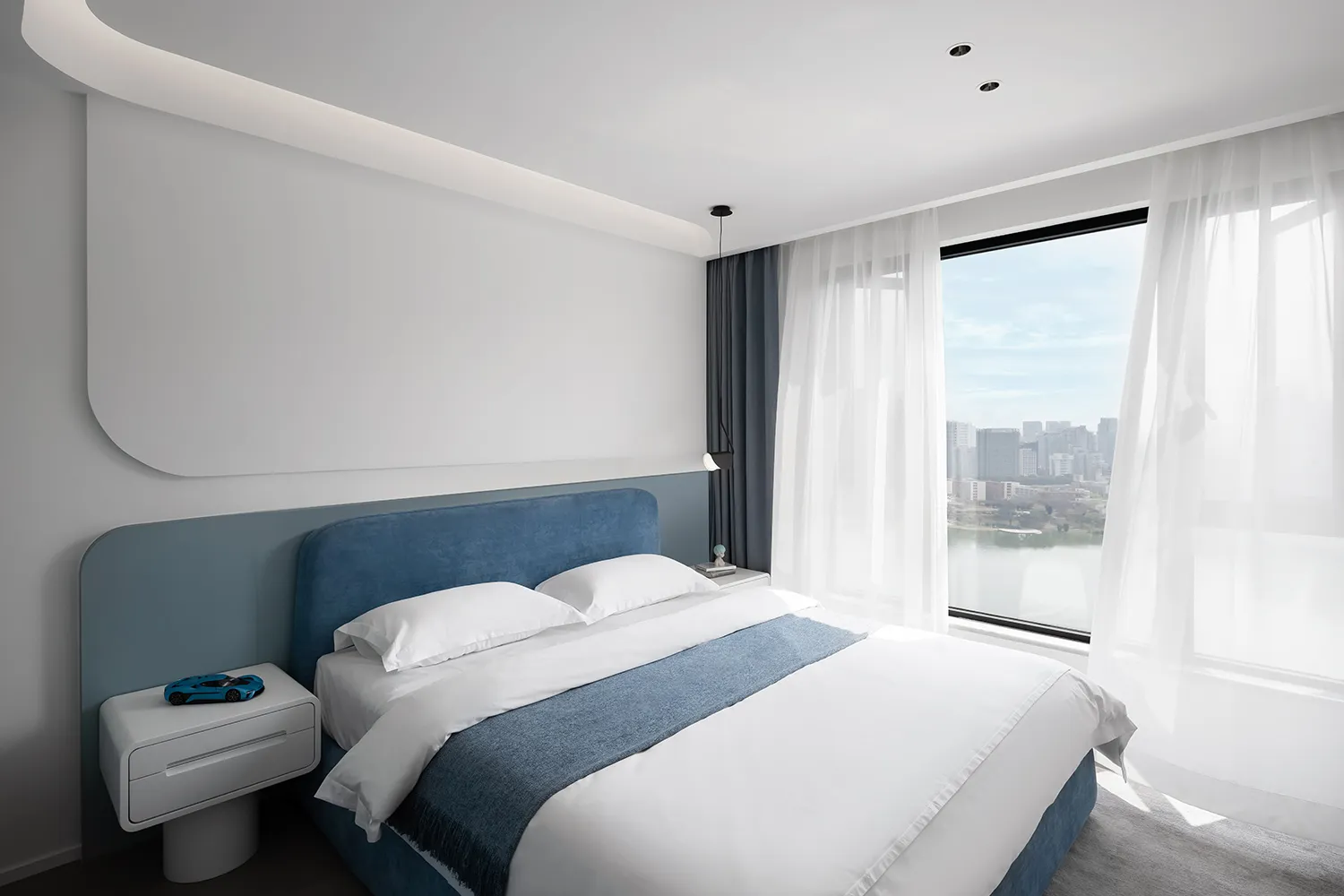 Modern minimalist bedroom featuring a blue upholstered bed with white bedding and a white bedside table with a small blue toy