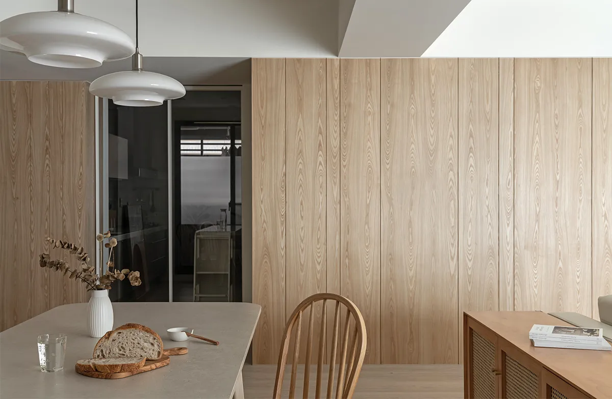 A minimalist kitchen featuring wooden timber walls and flooring, with a countertop displaying bread and a vase with dried flo