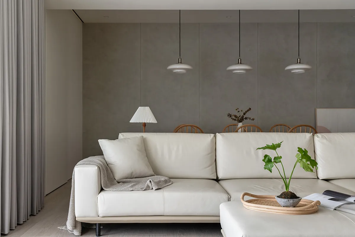 A modern living room featuring a white leather couch, a lamp, a small potted plant, and a tray with a book and a bowl.