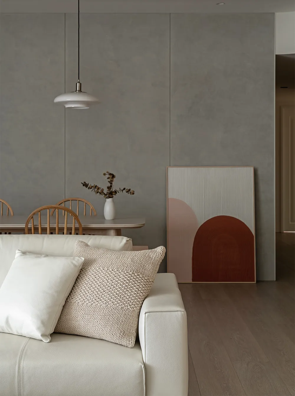 Modern living room featuring concrete walls and furniture, with a white leather sofa, wooden chairs, and abstract wall art.