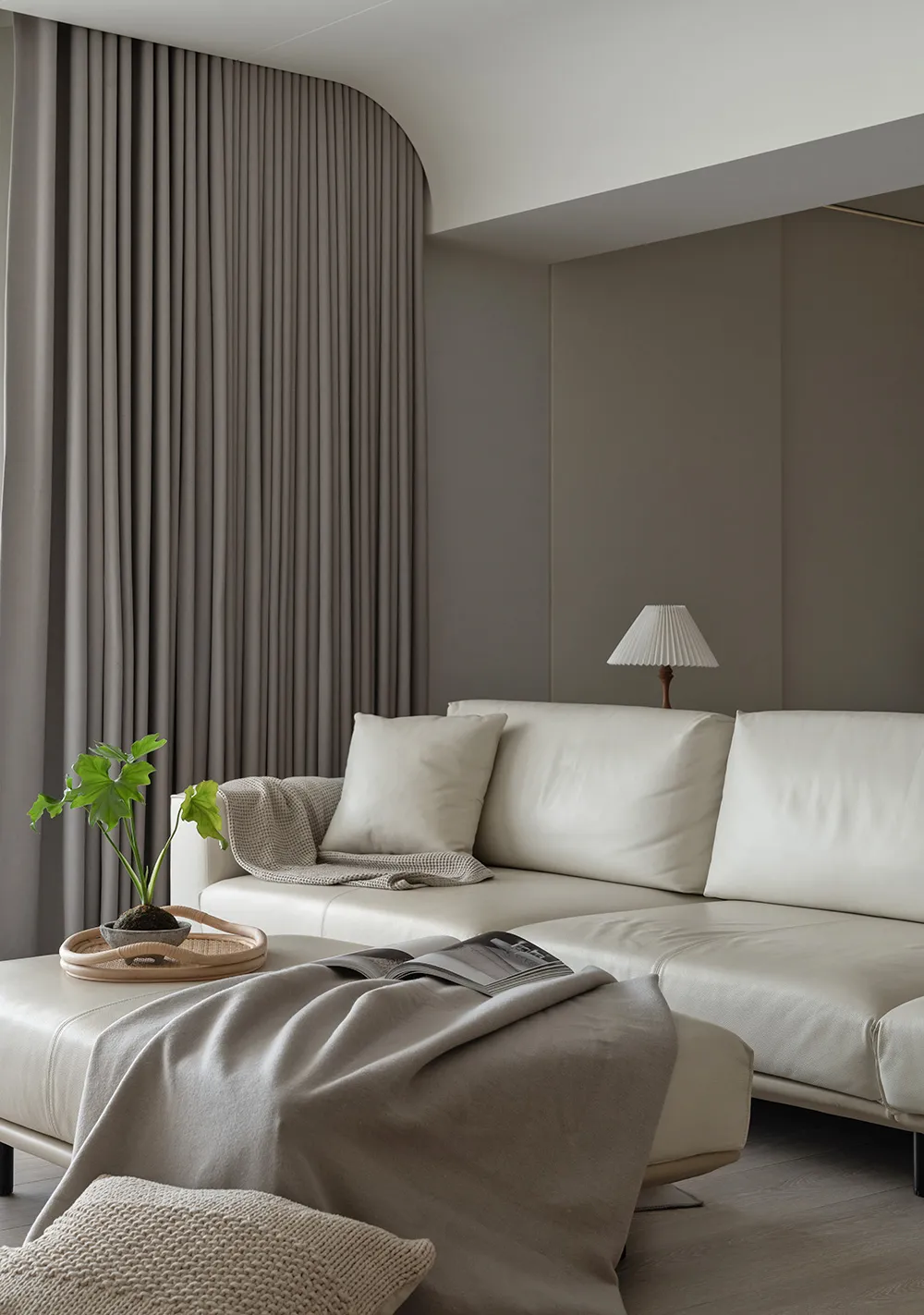 A minimalist living room featuring a couch, plants, and curtains.