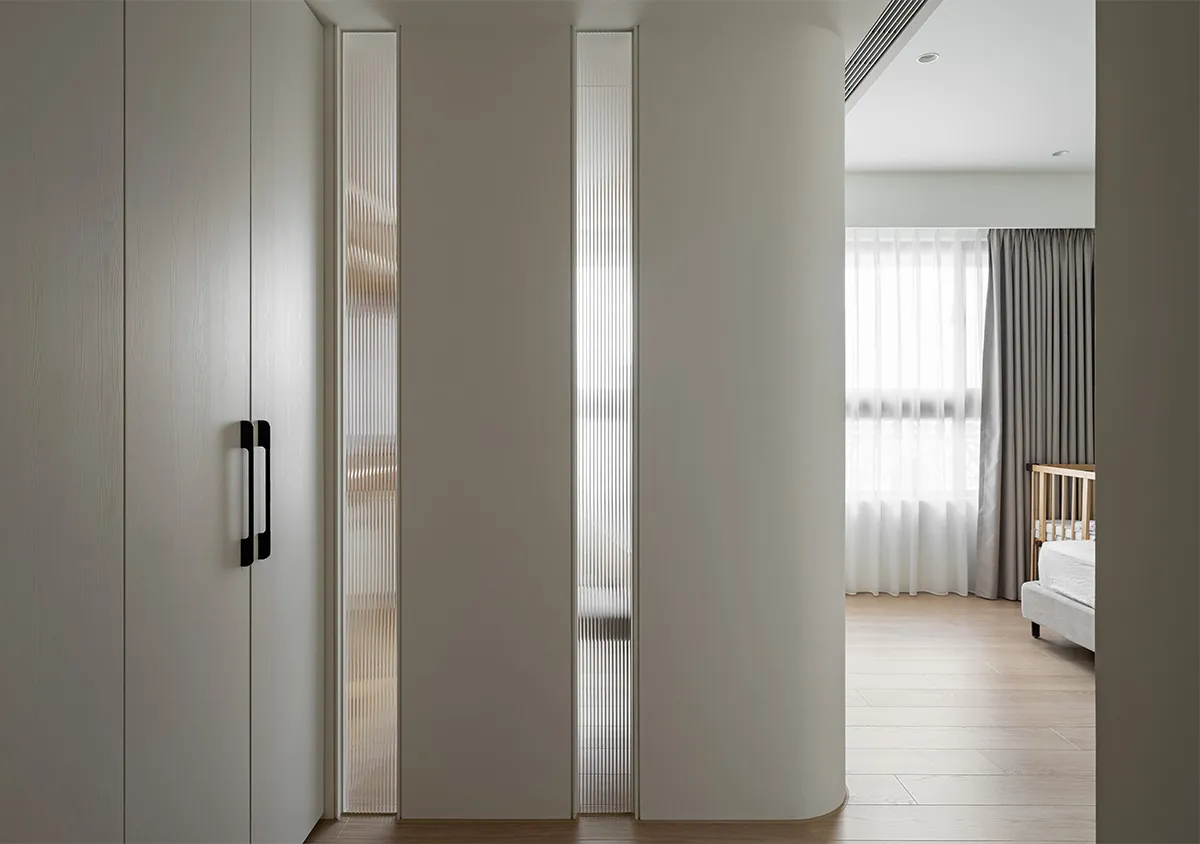 Modern minimalist bedroom featuring white cabinets, glass-paneled doors, and wooden flooring.