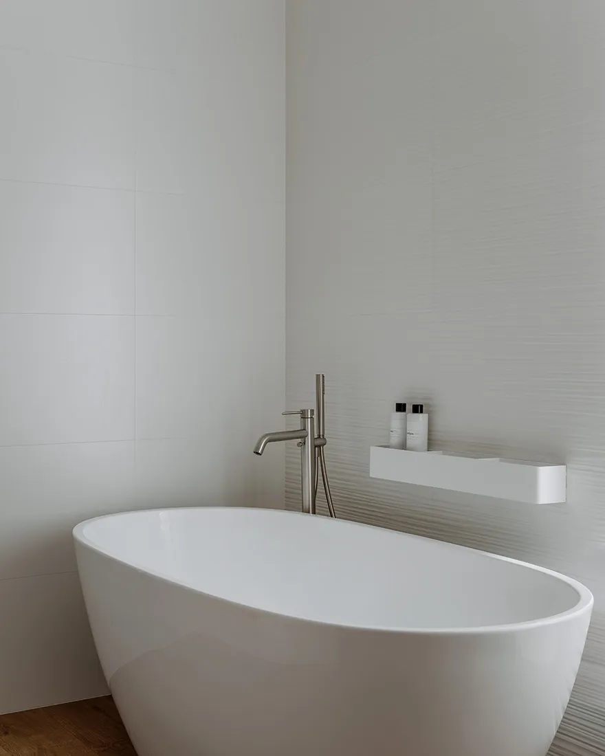 A modern bathroom with clean, white tiles and a sleek, white freestanding bathtub.