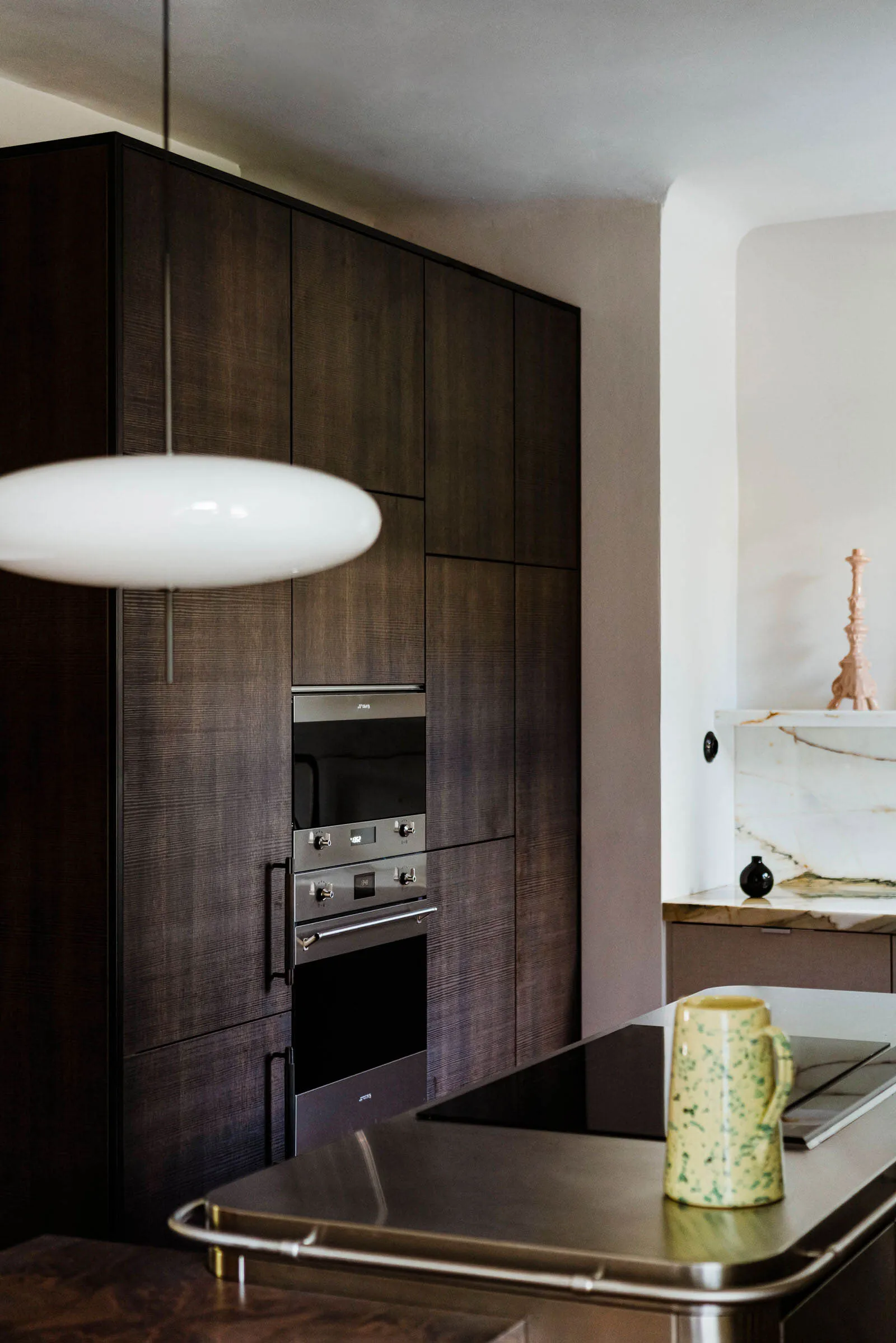 Modern kitchen with dark wood cabinets, stainless steel appliances, and a white pendant light.
