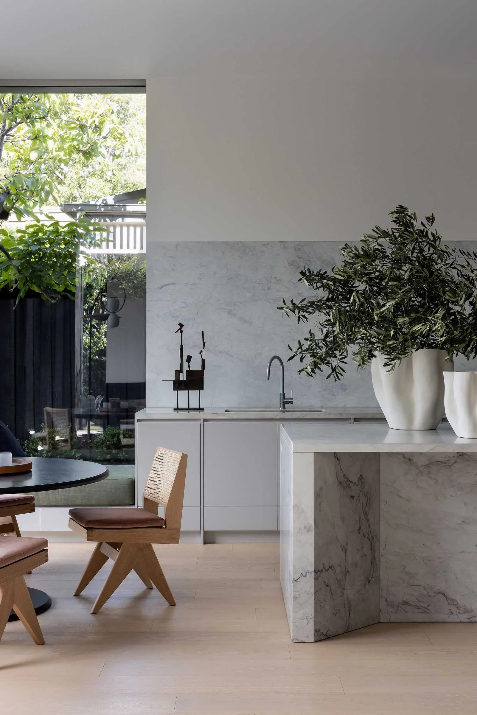 A contemporary kitchen with marble countertops and white cabinets, featuring a sleek sink and a large potted plant.