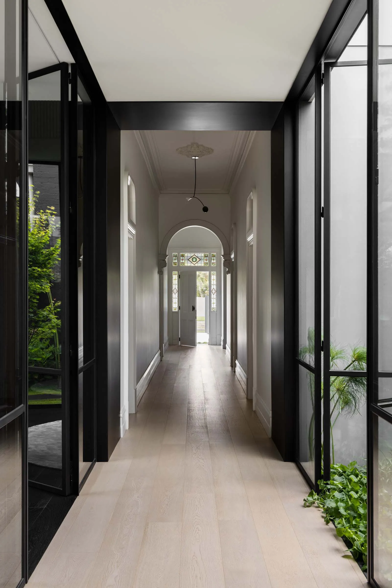 A modern minimalist hallway with light-colored wooden floors, clear glass panels, and white walls.