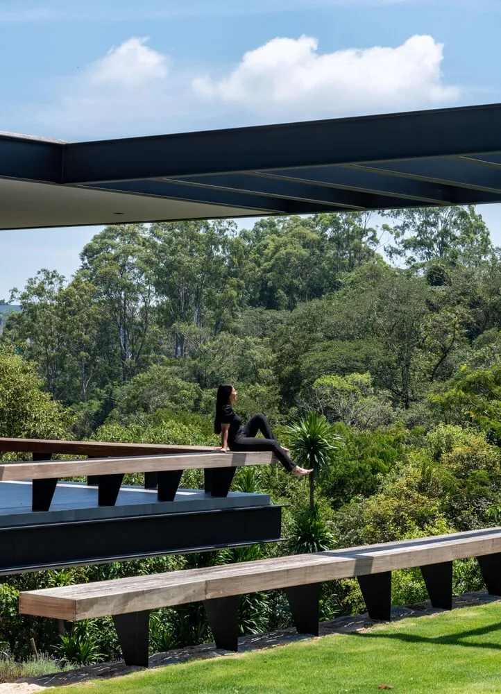 A woman sitting on a wooden bench overlooking a lush, green forest.