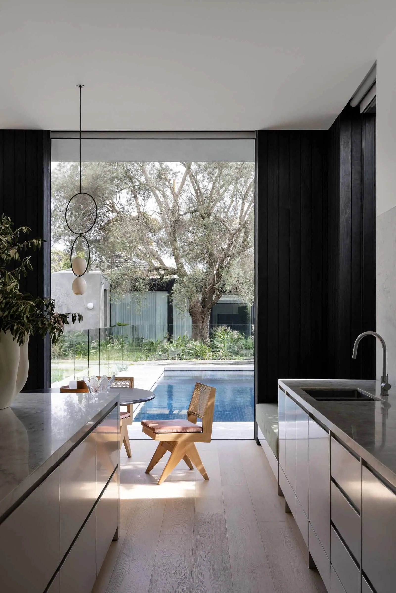 Modern residential kitchen featuring large glass windows overlooking a pool surrounded by trees.