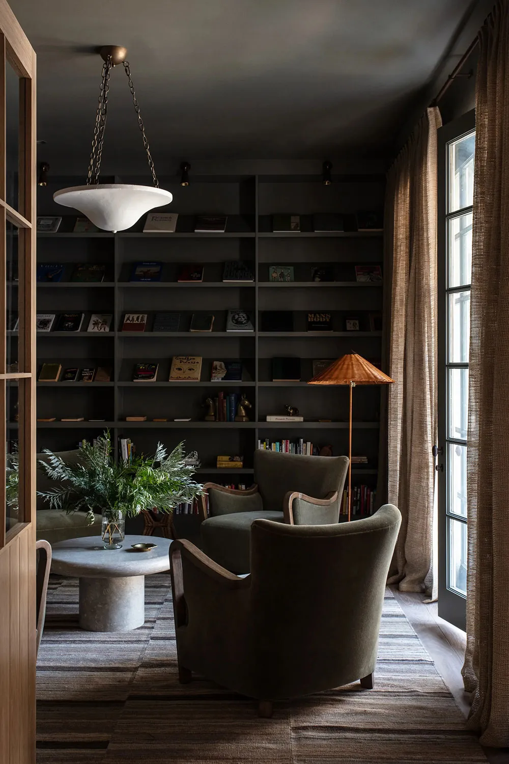 Industrial living room featuring plush green armchairs, glass lampshade, bookshelves, and green plants