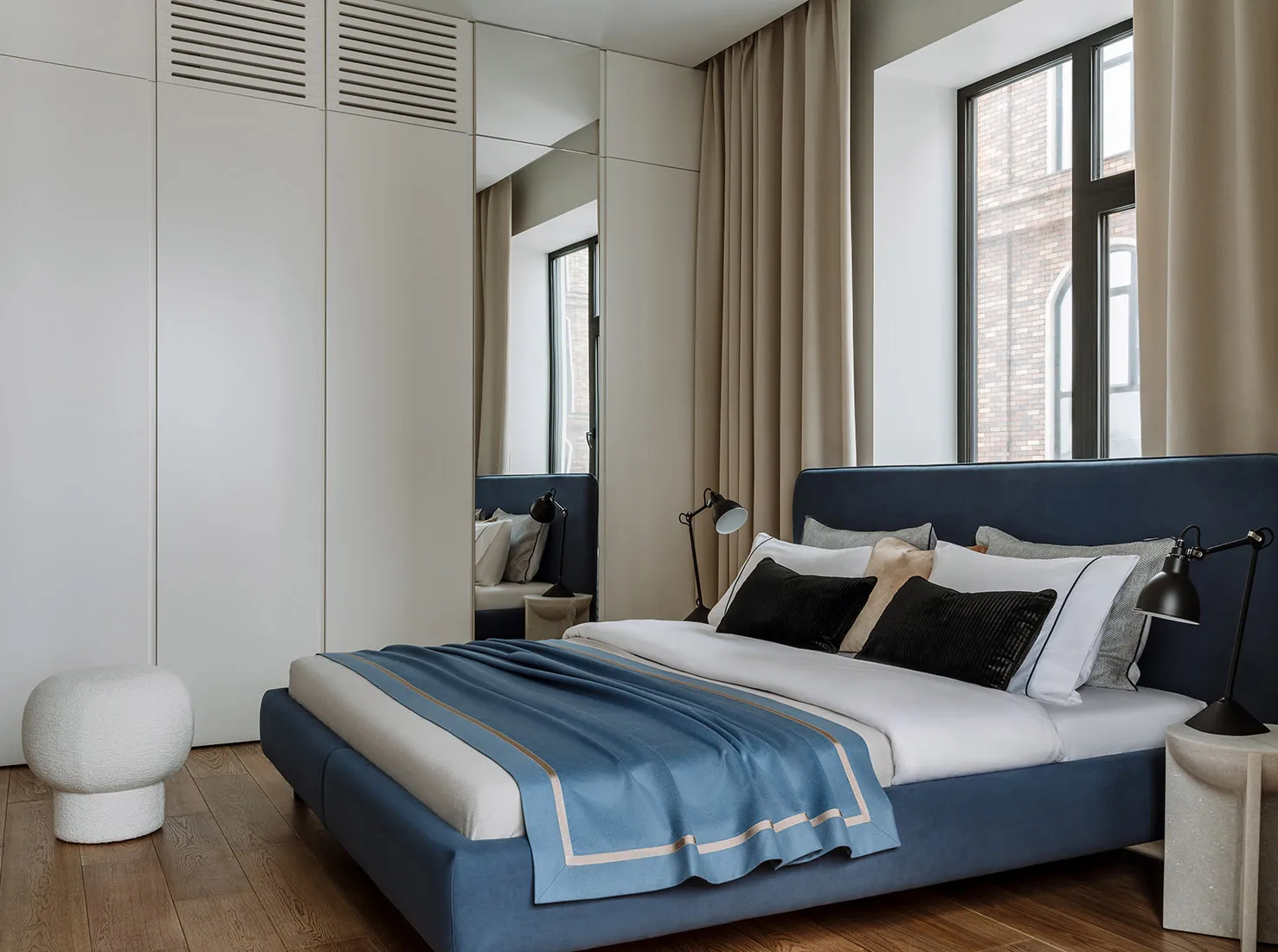 Modern minimalist bedroom with a blue upholstered bed, white linens, and black lamps.