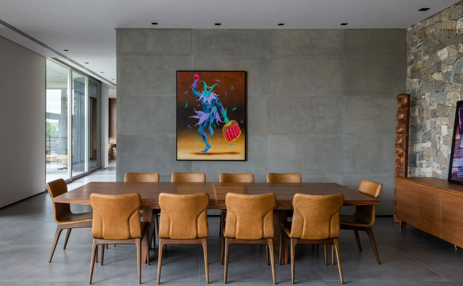 A modern dining room with concrete walls and a wooden dining table surrounded by brown leather chairs.