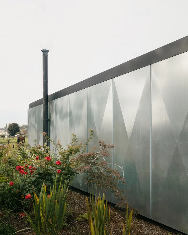 A modern exterior featuring a metal panel wall with a diamond pattern and a chimney.