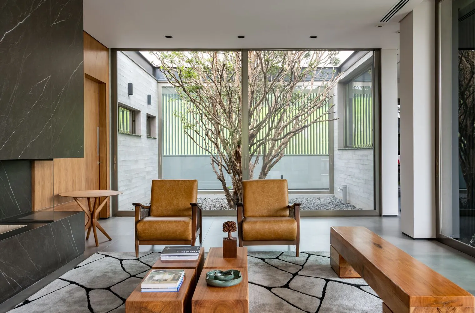 A minimalist living room featuring two brown leather armchairs, a marble side table, and a wooden bench.