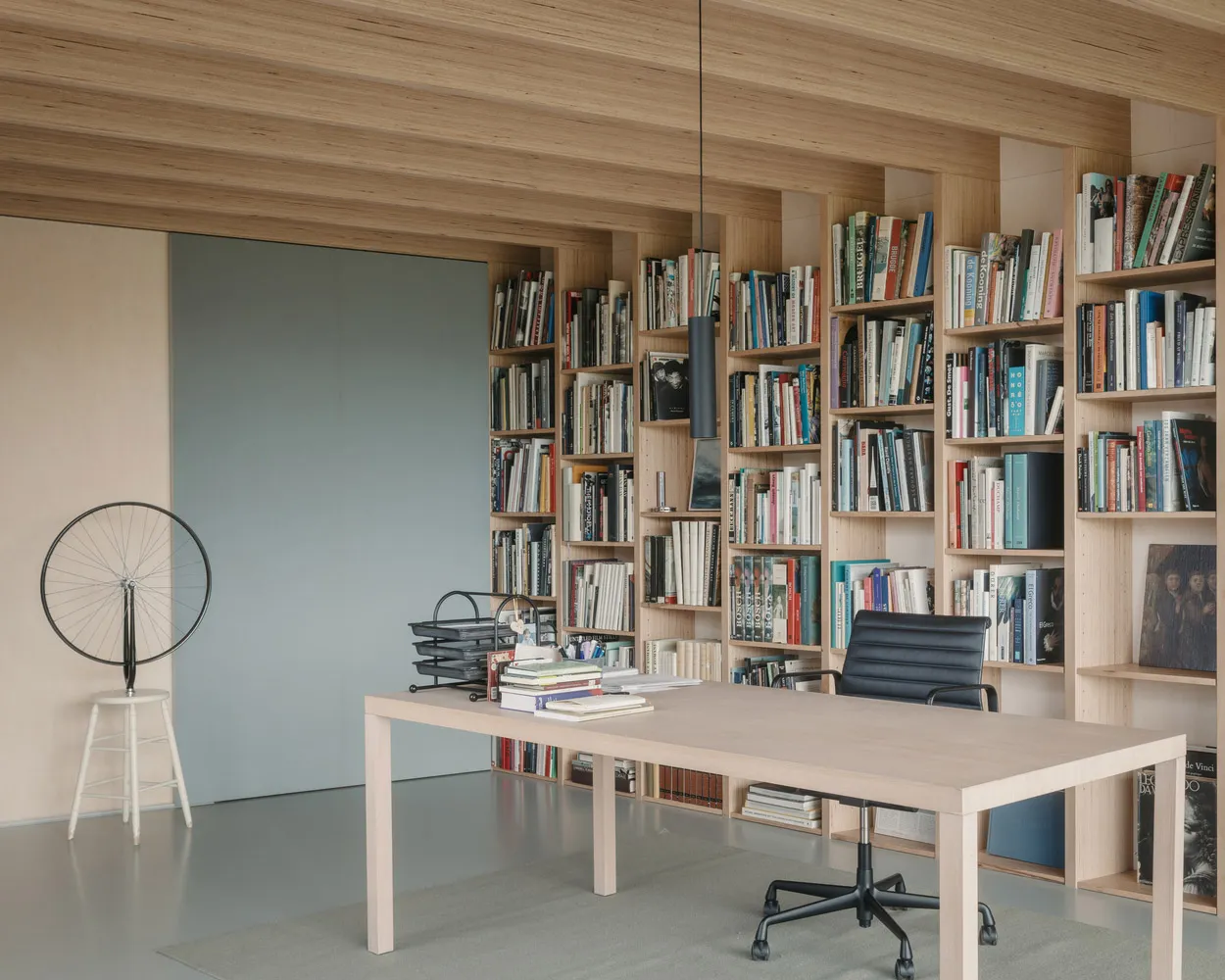 A modern home office featuring a wooden desk, bookshelves filled with books, and a black office chair.