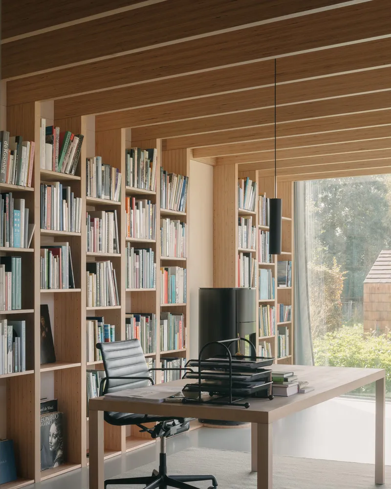A modern library office space featuring timber bookshelves and a desk with a black chair.