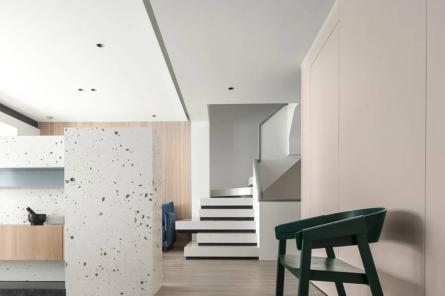 A modern residential interior featuring a white speckled wall, white and black stairs, and a green chair in a simple, clean s