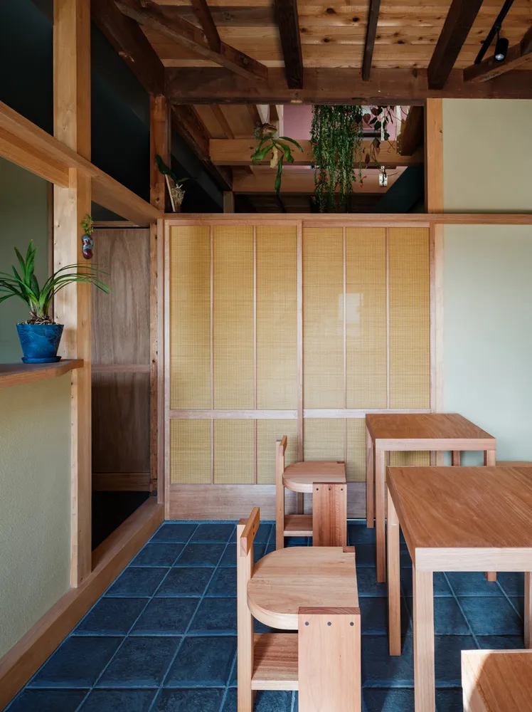 A modern restaurant interior with wooden furniture and plants on shelves.