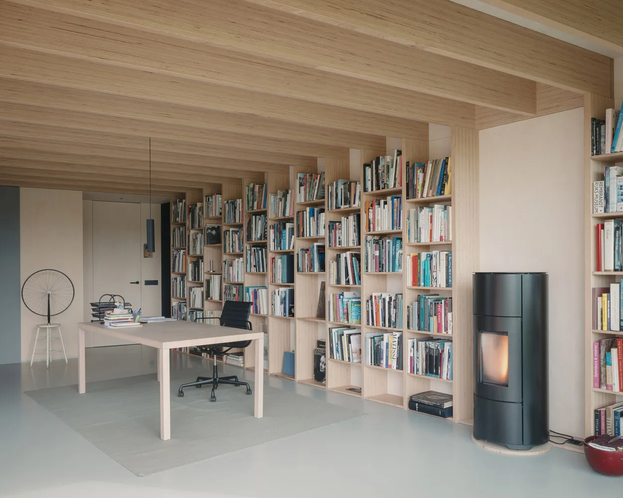 A modern home office featuring wooden walls and bookshelves filled with books.