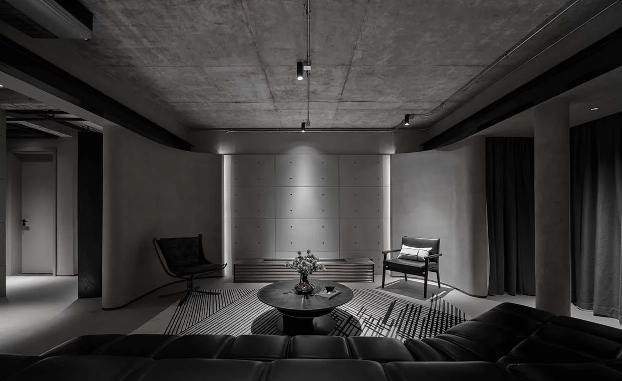 Modern industrial-themed living room with concrete walls and black leather furniture.