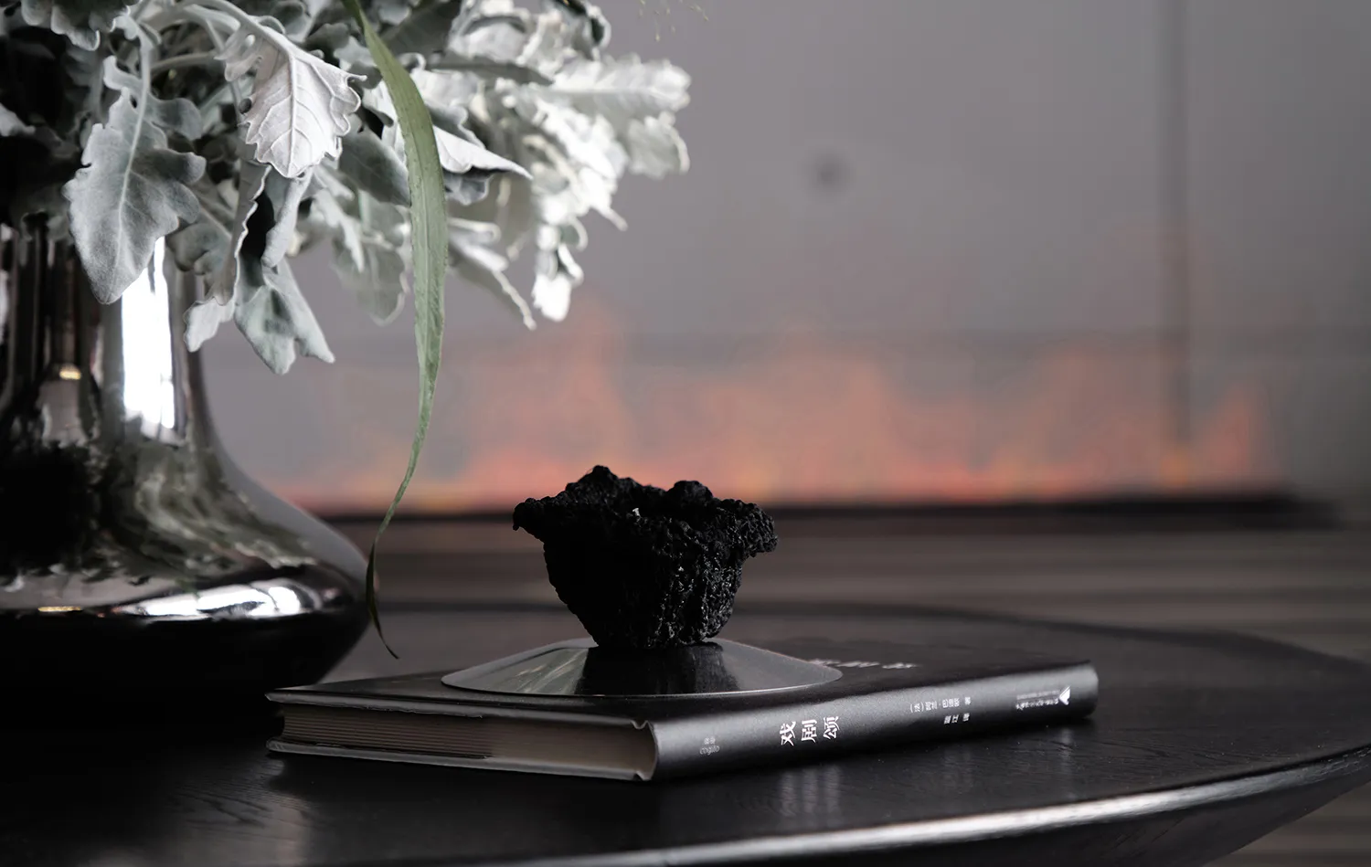A minimalist interior decor setup featuring a metallic vase with a flower arrangement and a black book with a black ceramic o
