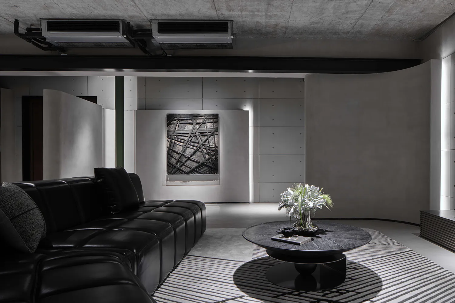 A modern living room with a black leather sectional sofa, abstract art, and a round wooden coffee table with a plant.
