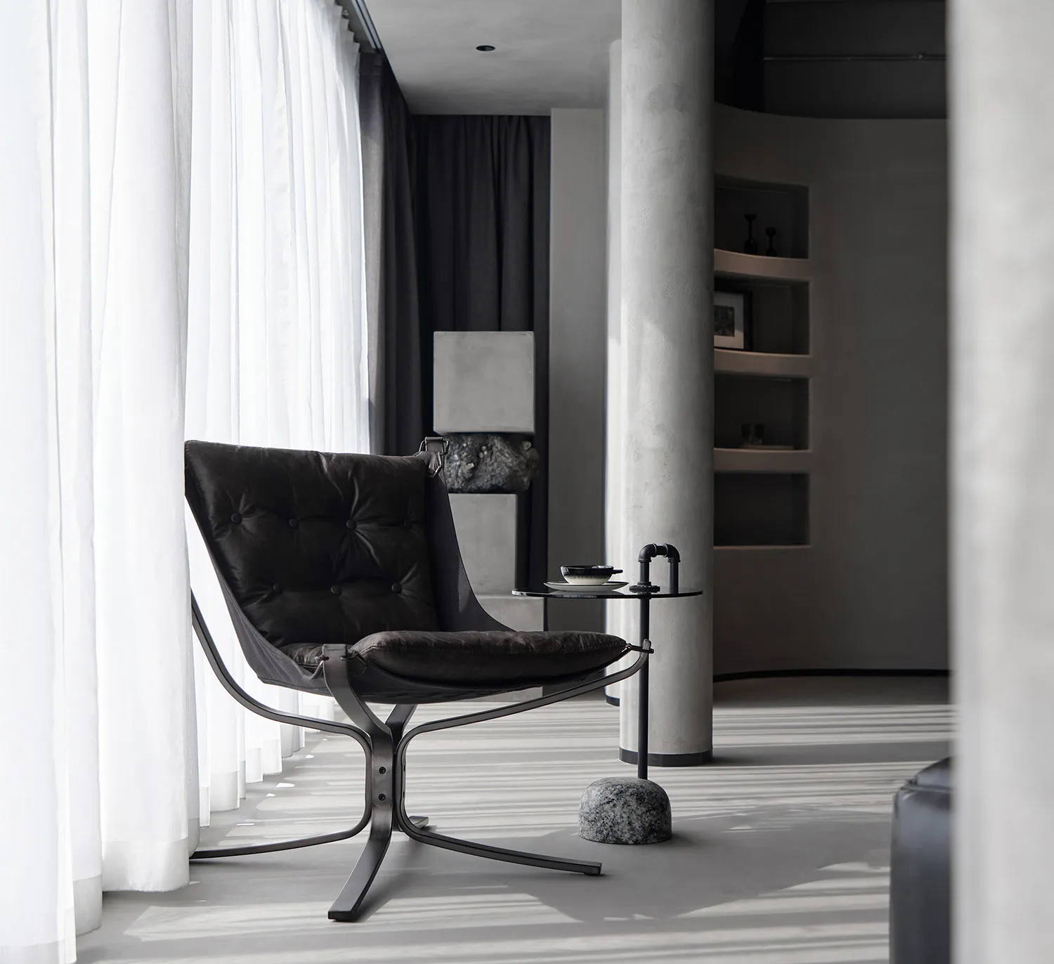 Modern room featuring a black leather chair, metal table, and concrete floor.