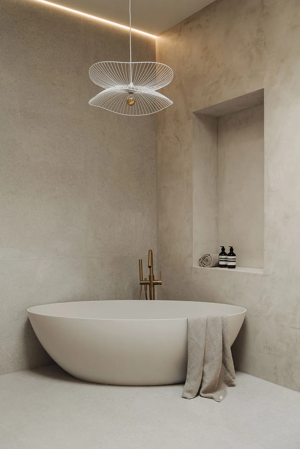 A minimalist bathroom interior with a freestanding bathtub, modern lighting fixture, and concrete walls.