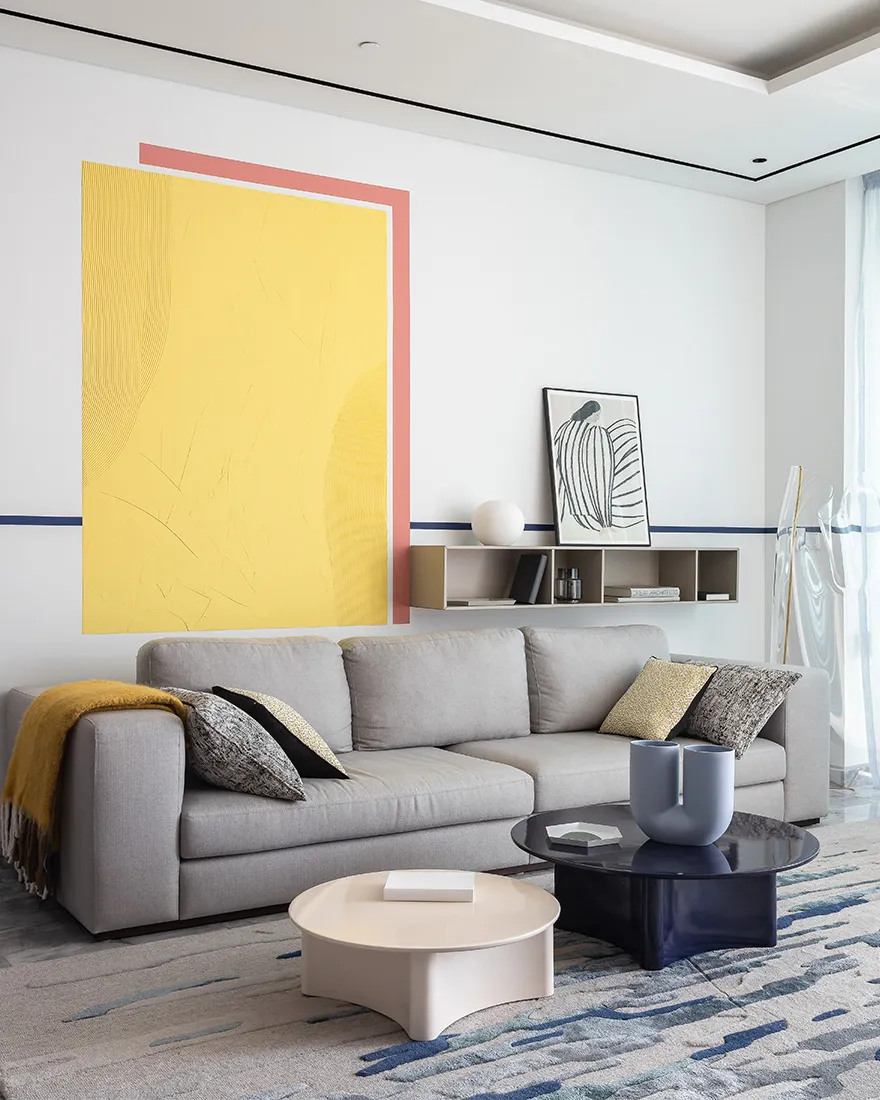 A minimalist living room featuring a gray couch with patterned pillows, a round coffee table, and abstract art on the wall.