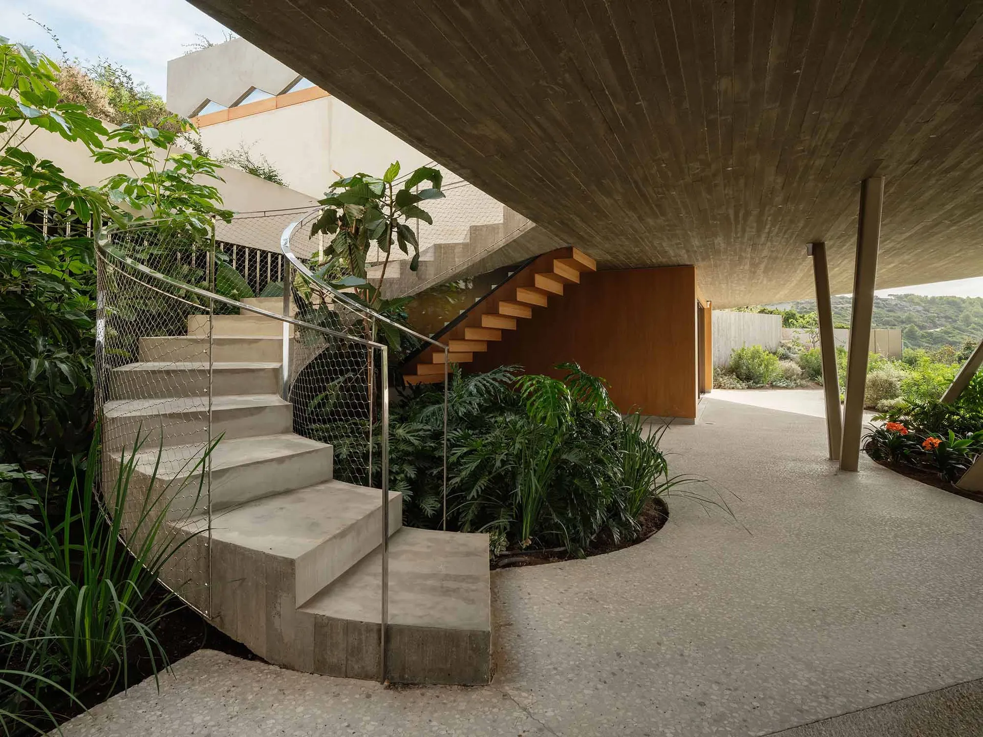 Concrete stairs leading to a wooden staircase surrounded by green plants