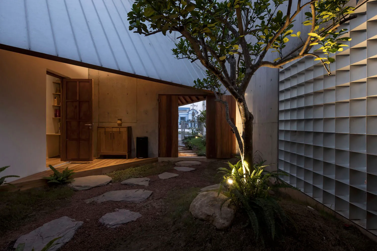 A modern, minimalist backyard with concrete elements, plants, and a tree.