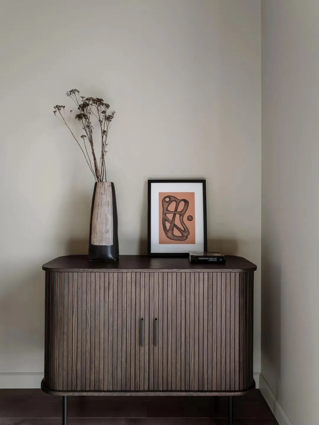 A minimalist cabinet with wooden doors and a vase with dried flowers.