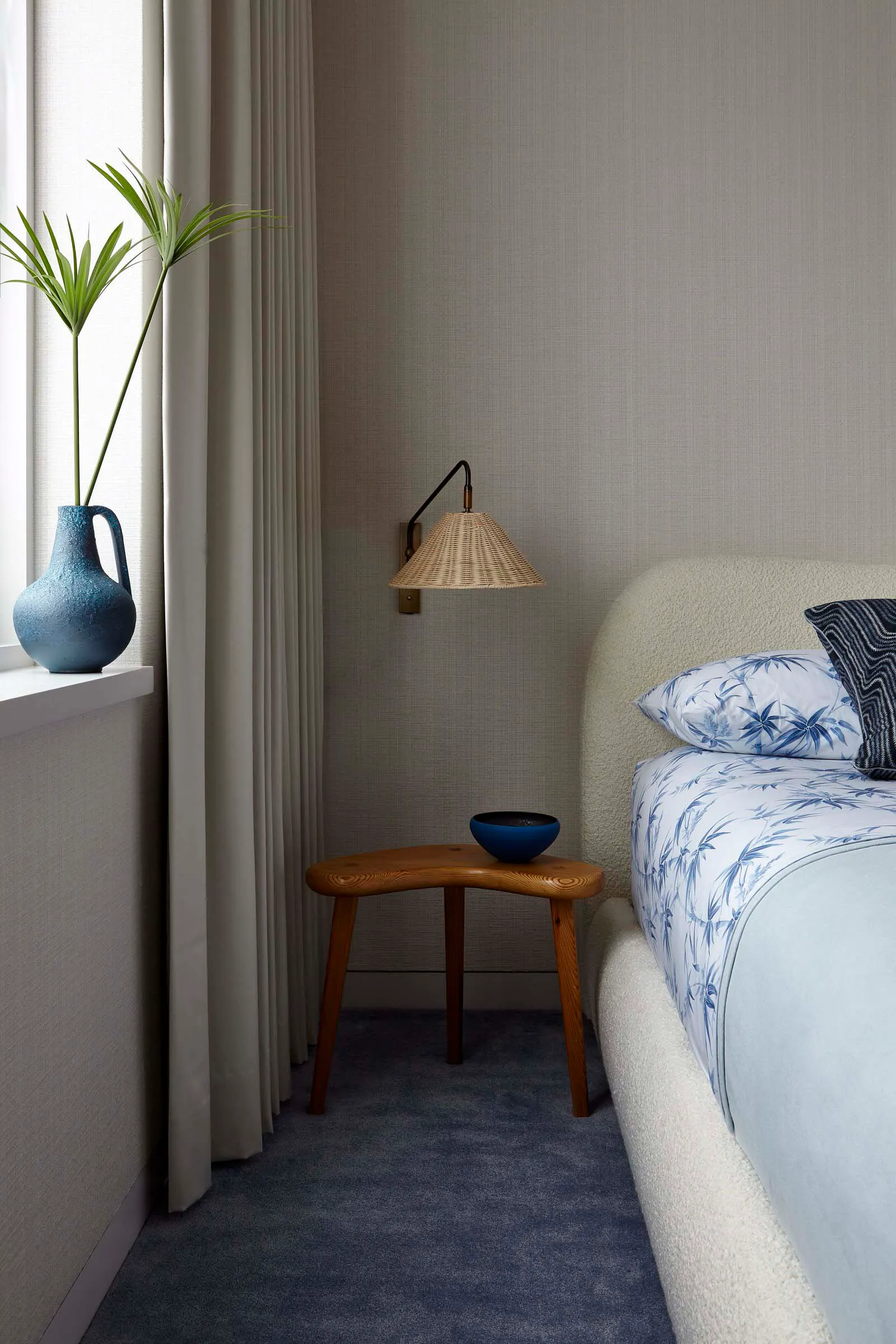 A minimalist bedroom featuring a bed with a white fabric headboard and a blue floral quilt, accompanied by a wooden bedside t