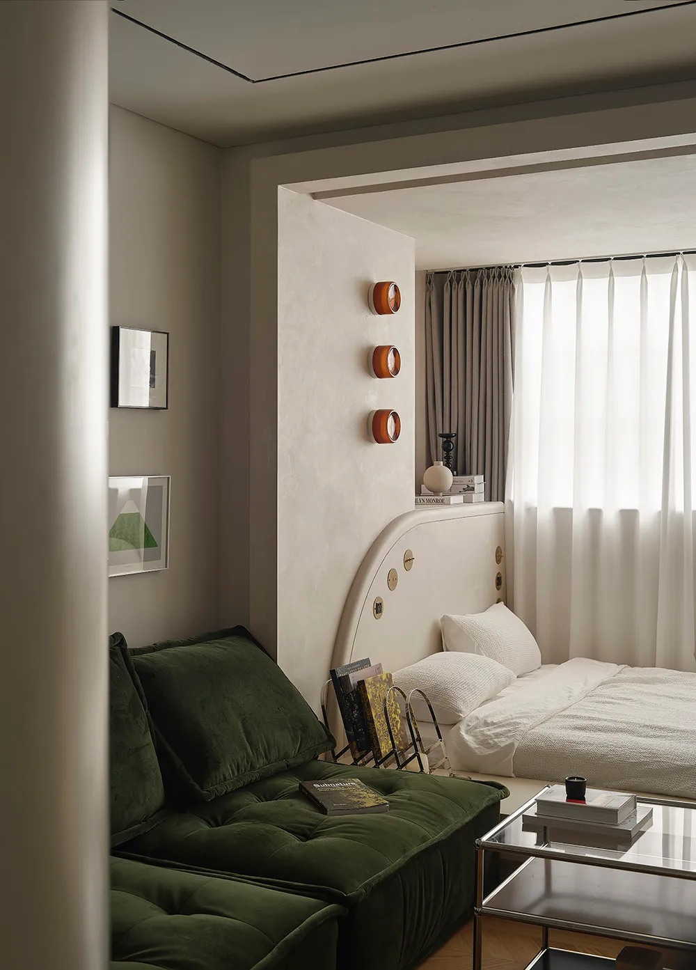 A modern bedroom featuring a bed with a fabric headboard and a glass coffee table with books and a candle.