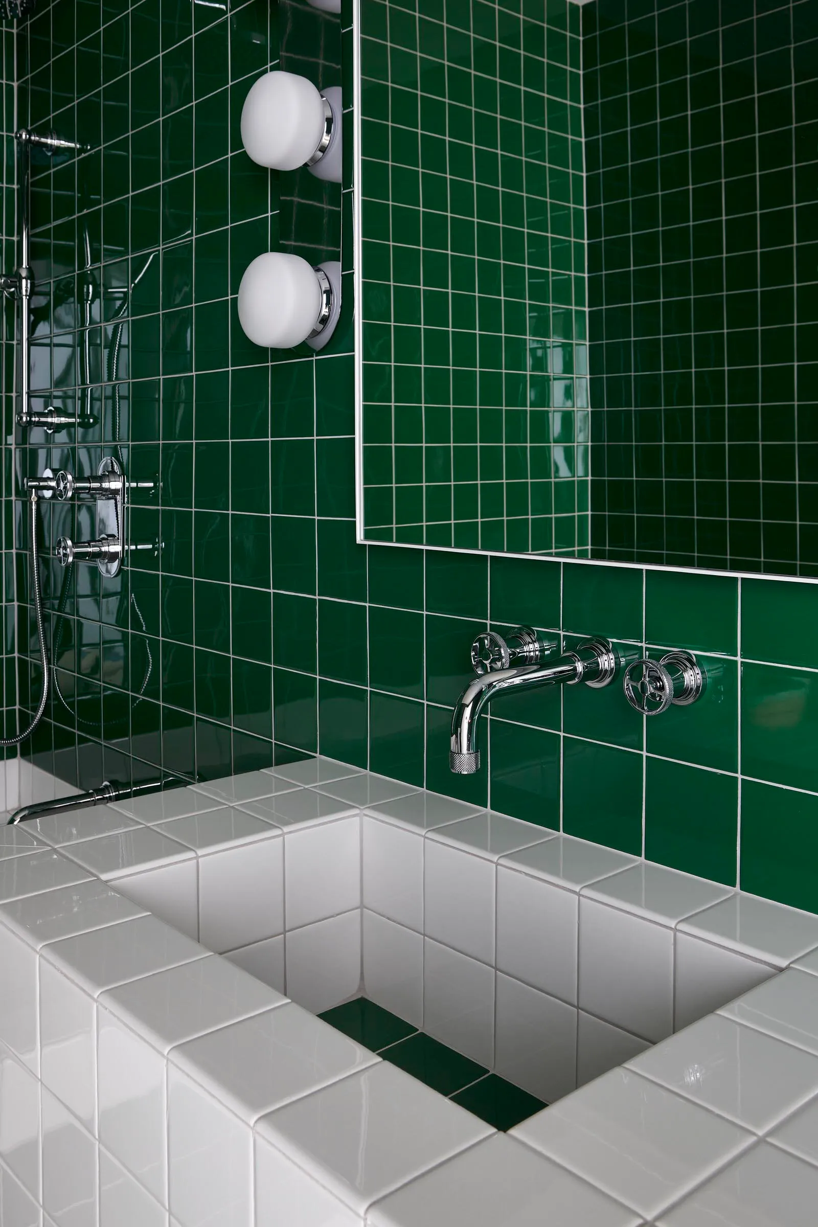 A modern bathroom with green-tiled walls, a white sink, and chrome fixtures.