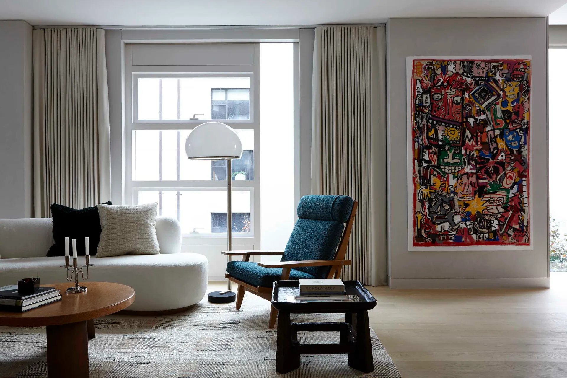 A modern minimalist living room with a white sofa, blue armchair, and abstract art on the wall.